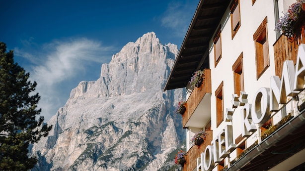 A hotel with a mountain backdrop, wooden balconies with flower boxes, and a clear sky.