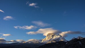 A mountain landscape with a prominent peak, forested slopes, and a clear sky.