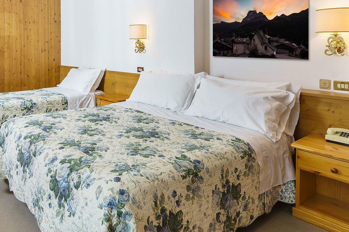 A hotel room with two beds, wooden furniture, a desk, and a painting of a mountain scene.