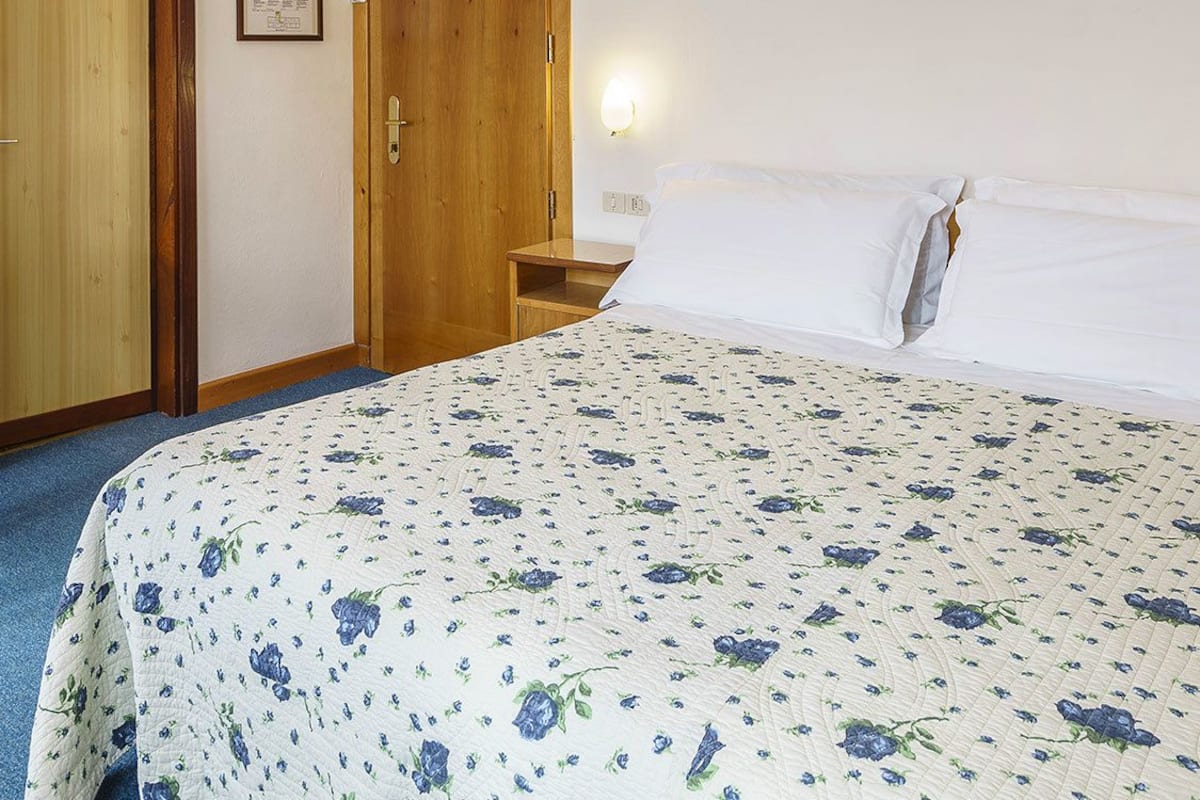 A bedroom with a bed, a desk with a chair, a nightstand, and a wall-mounted lamp.