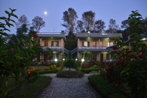 Un hotel con edificios de dos pisos, una escalera central y un jardín con senderos de grava y plantas en flor.