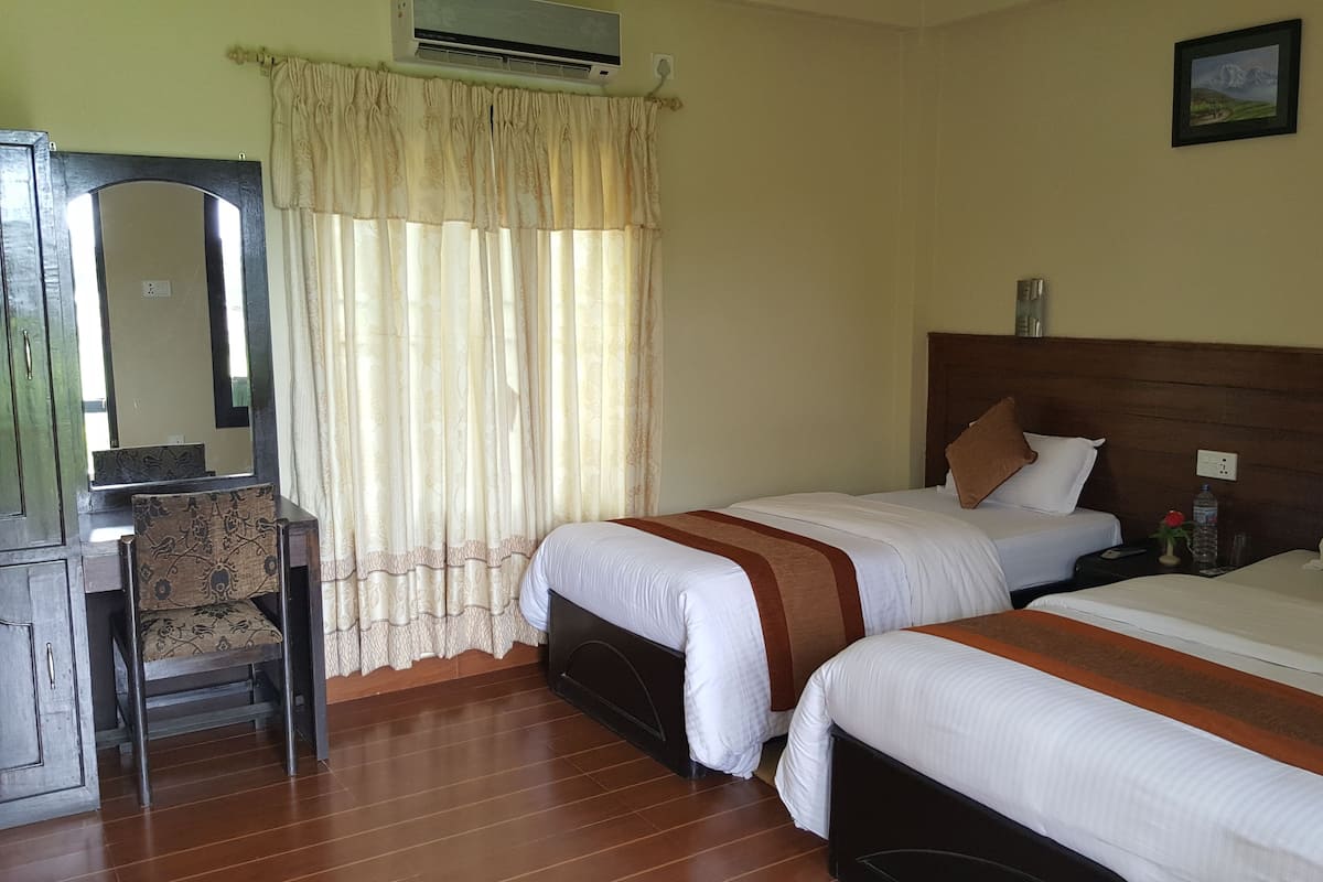 A hotel room with two beds, a desk, a chair, and an air conditioning unit.