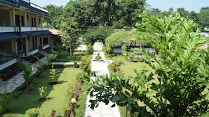 A courtyard with a stone pathway, surrounded by lush greenery and a building with a balcony.