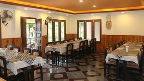 A dining area with multiple tables and chairs, wooden paneling on the walls, and ceiling fans.