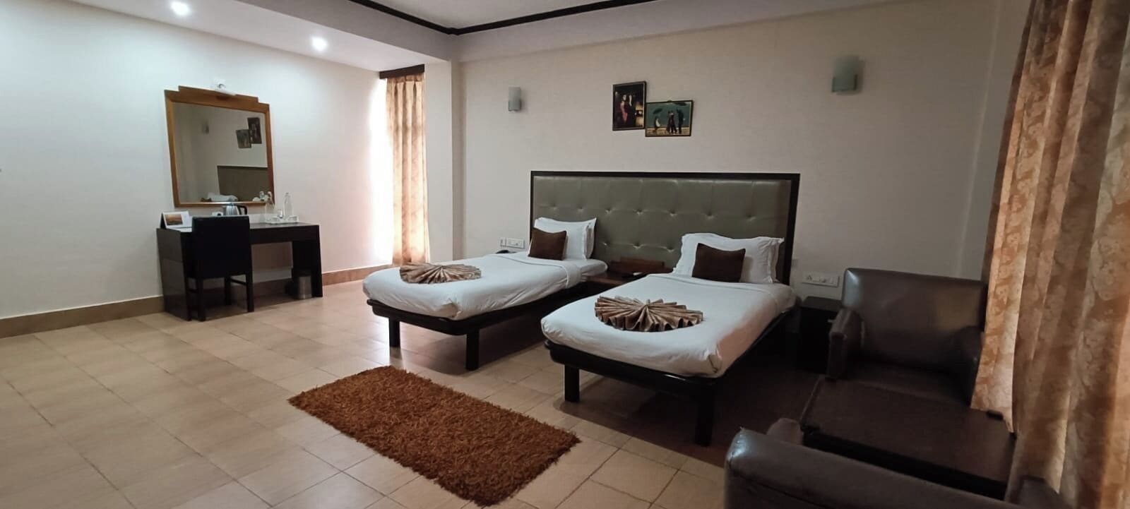 A hotel room with two single beds, a desk with a chair, a large mirror, and a brown rug.