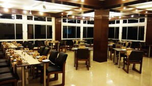 A large dining hall with long tables and chairs, large windows, and a polished floor. - Polo Tura Hotel (West Garo Hills)