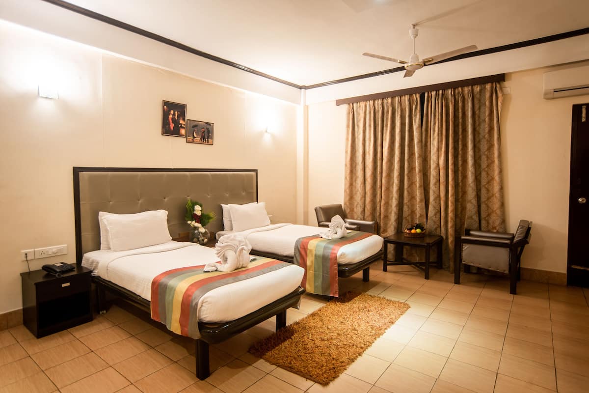 A hotel room with two beds, a nightstand with a phone, a desk with a chair, a ceiling fan, and a window with curtains.