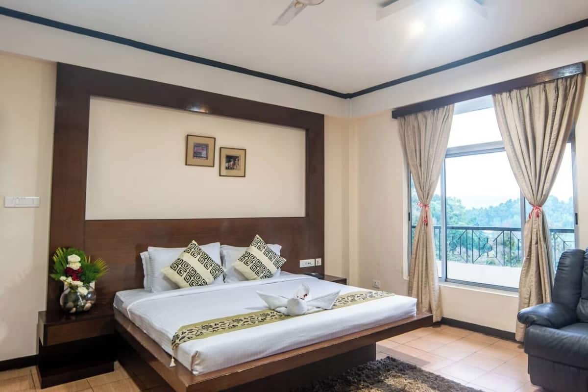 A bedroom with a large bed, a black leather chair, and a window with curtains.