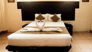 A hotel room with a neatly made bed, a black headboard, and two nightstands with lamps. - Polo Tura Hotel (West Garo Hills)