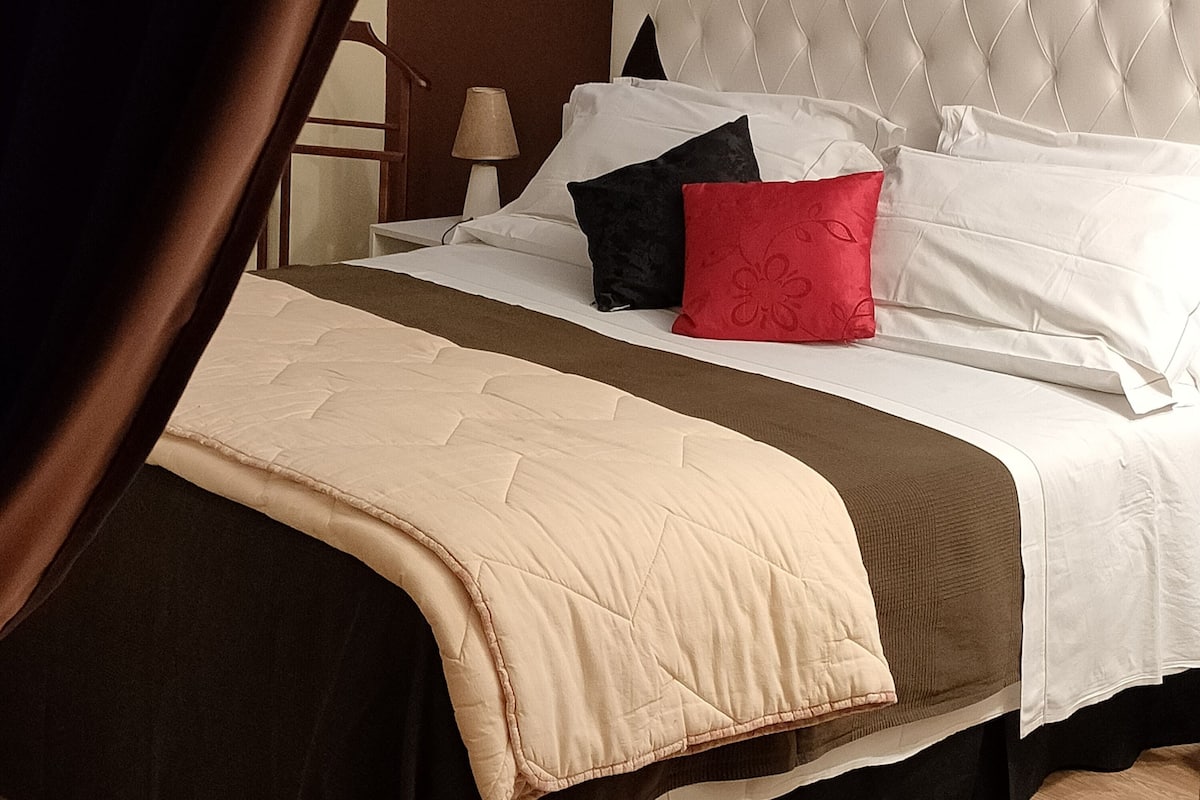 A neatly made bed with a tufted headboard, a bedside lamp, and a window with curtains.