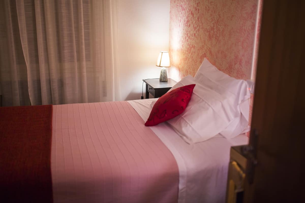 A hotel room with a bed, a nightstand, a lamp, and a window with curtains.