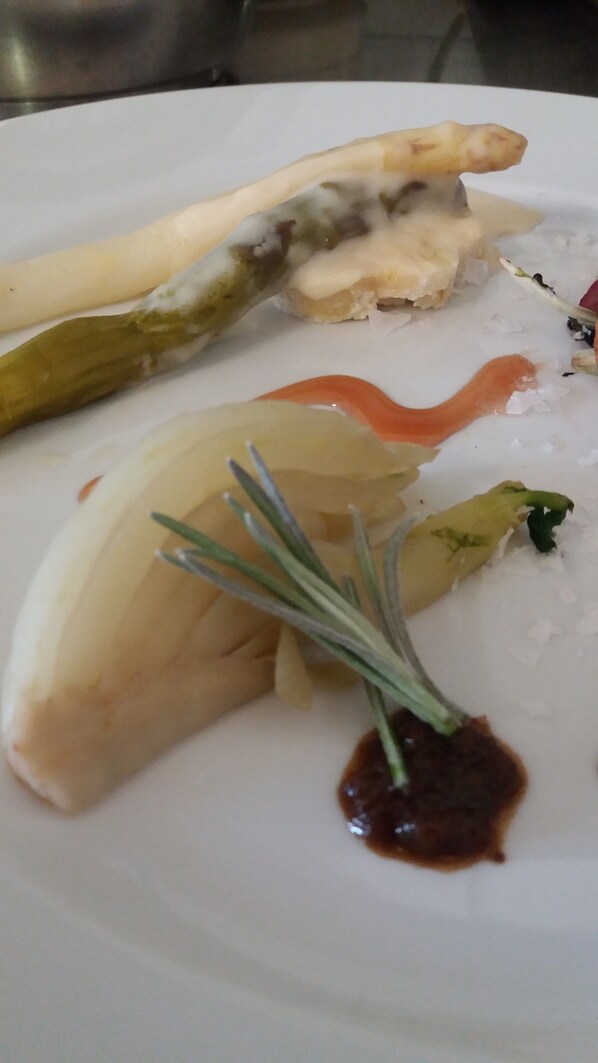 A white plate with a piece of fish, a green vegetable, and a small sprig of rosemary. - Quari Hotel Restaurant & Pizza (Cologna Veneta)