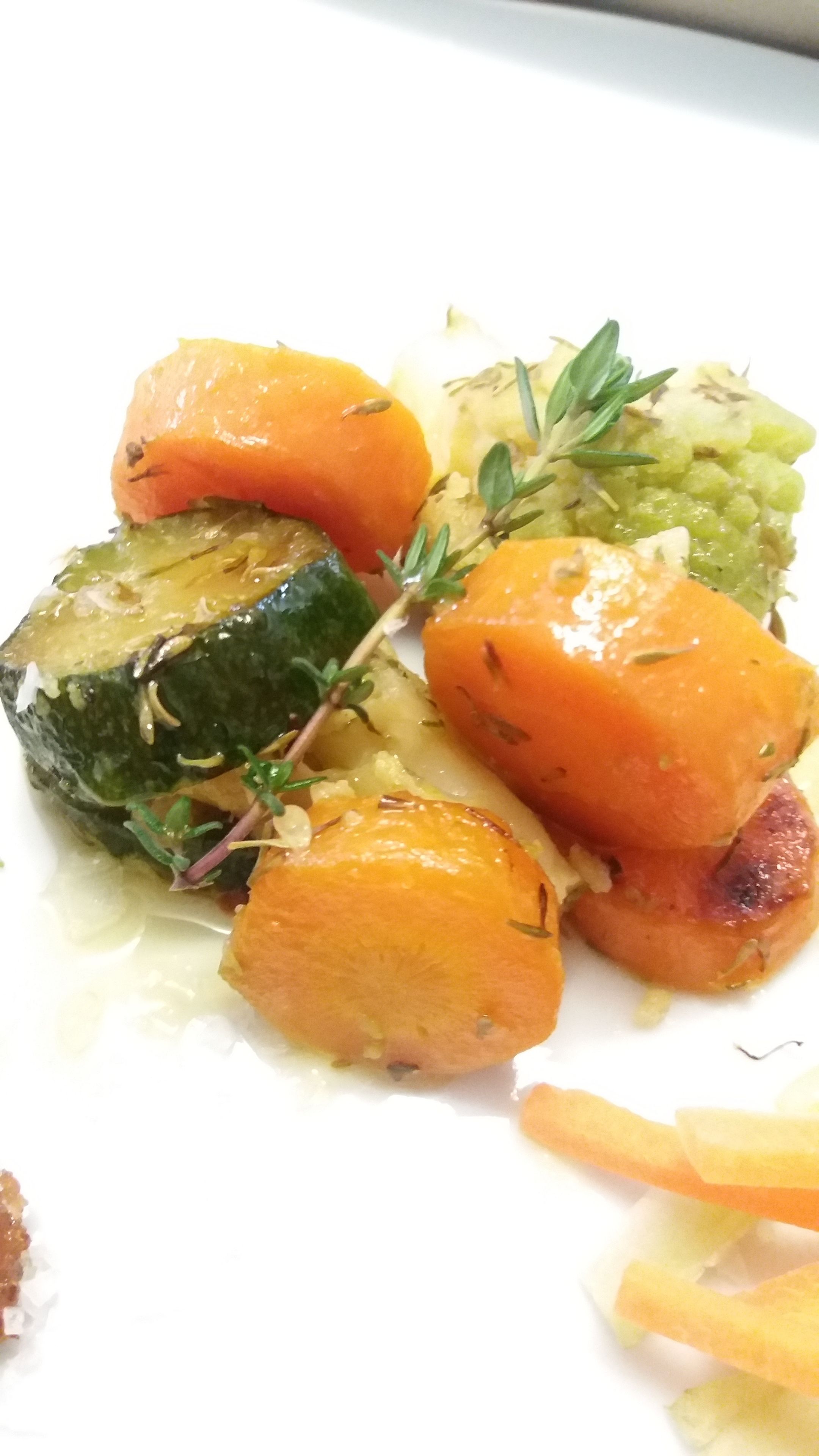 A plate of roasted vegetables including carrots, zucchini, and possibly eggplant, garnished with herbs.
