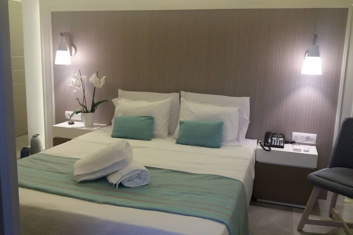 A hotel room with a neatly made bed, two bedside tables, a chair, and a telephone.