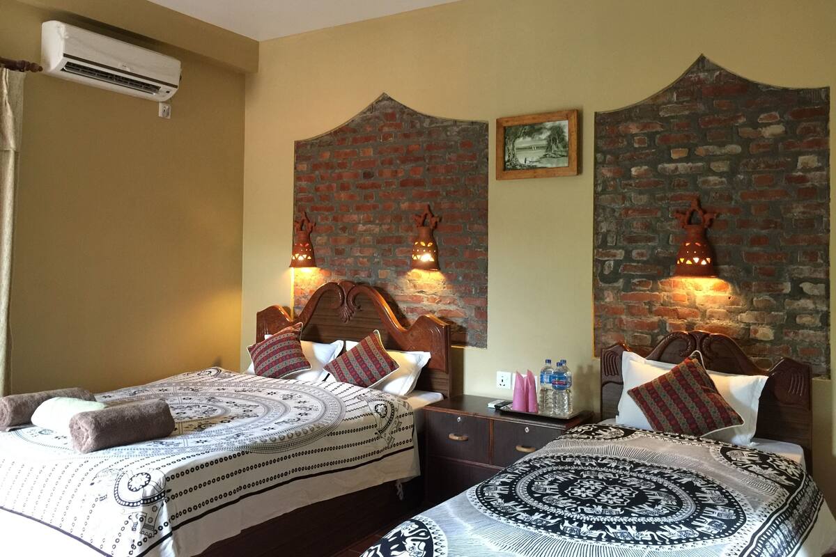 Une chambre d’hôtel avec deux lits, un mur en briques, un climatiseur fixé au mur et des lampes fixées au mur.