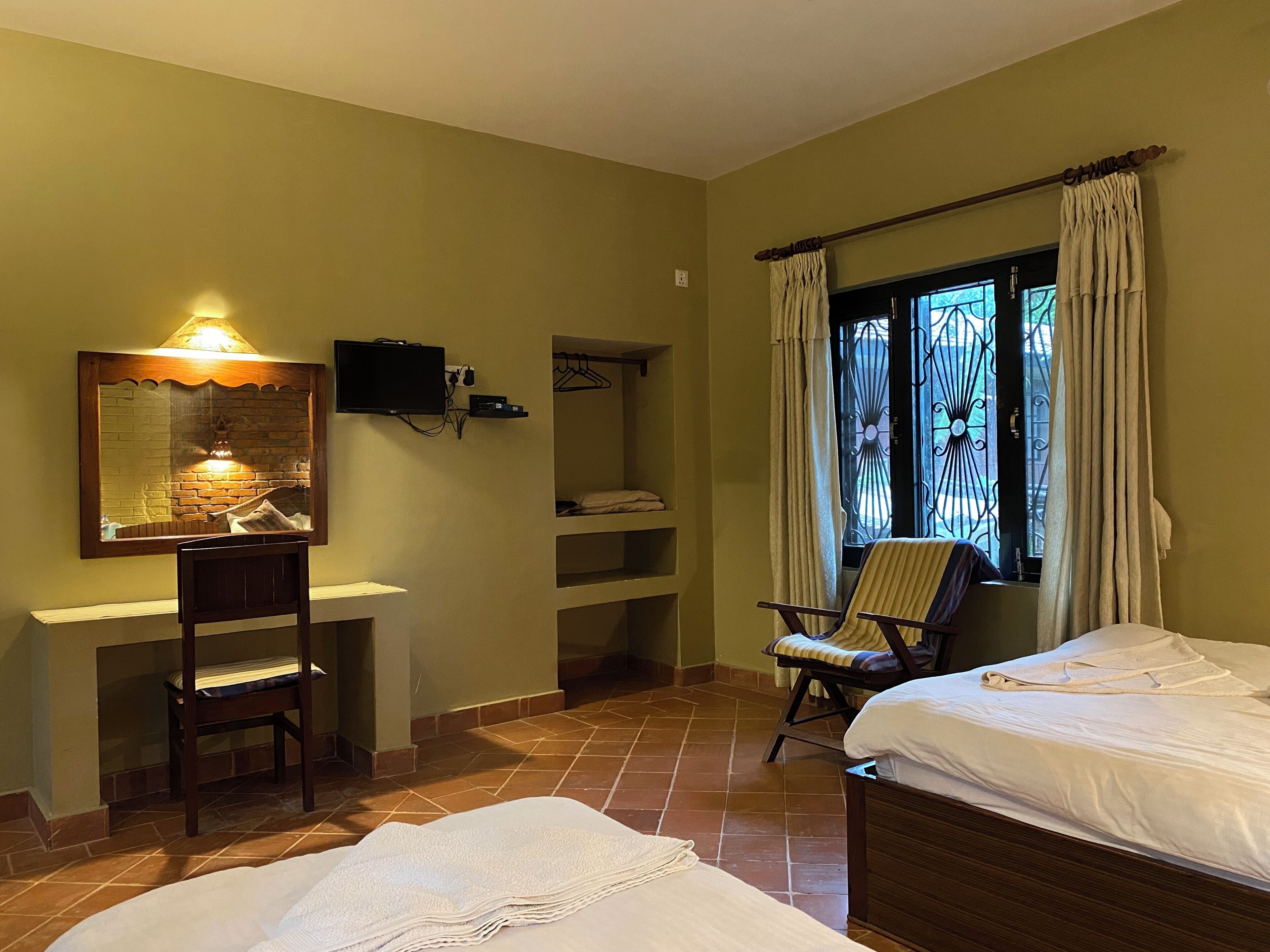 A hotel room with two beds, a desk with a chair, a TV, and a window with curtains.