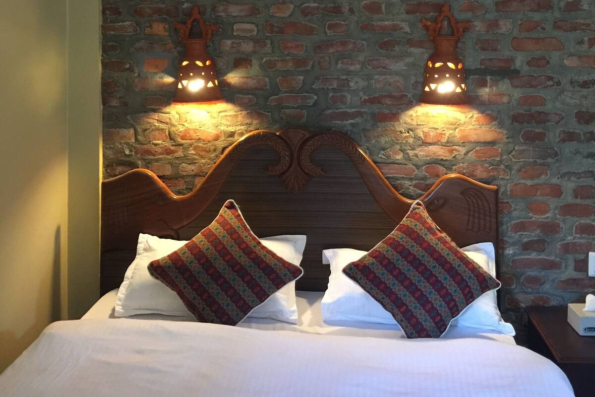 Un lit avec une tête de lit en bois, deux lampes fixées au mur et un mur en briques.