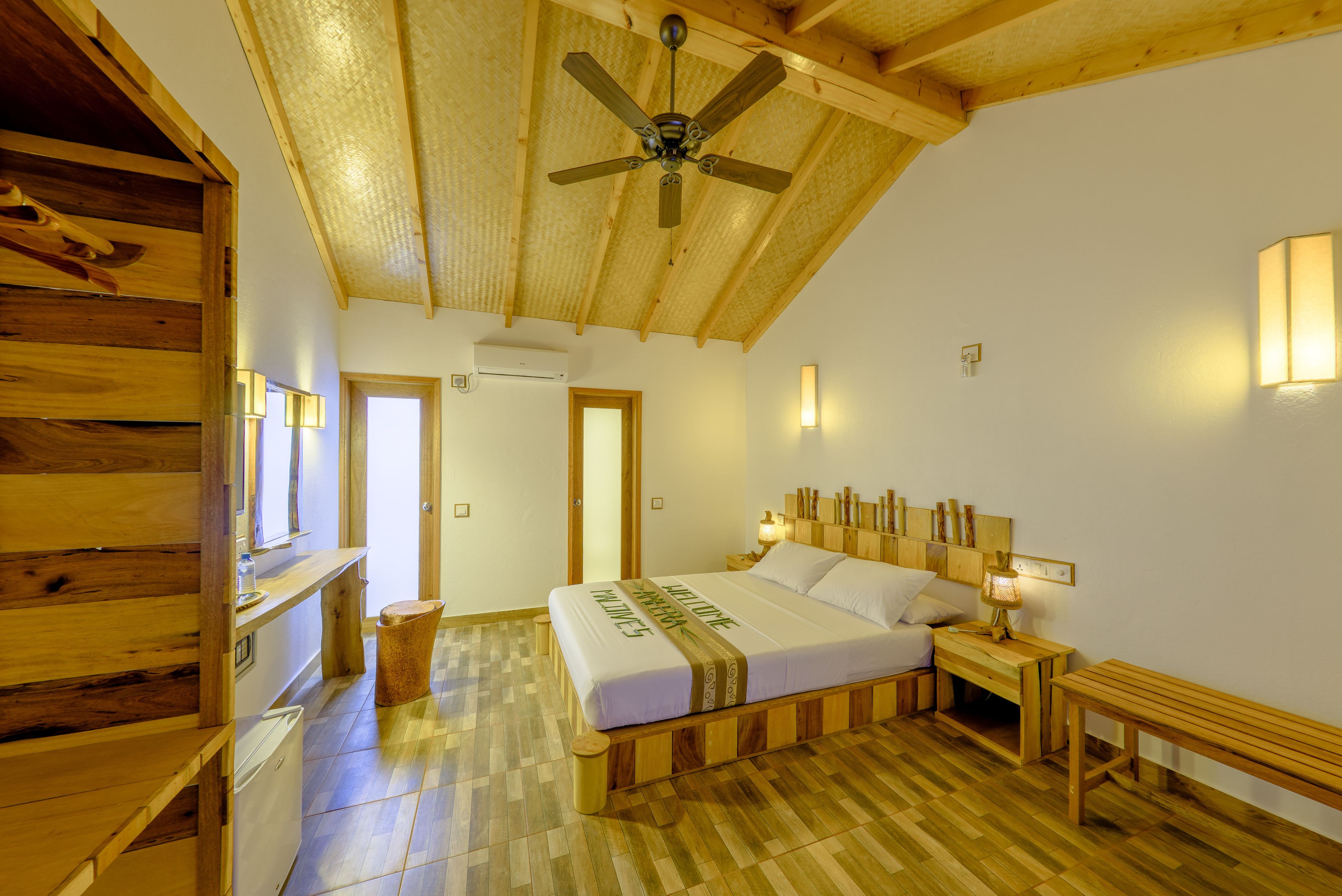 A wooden-floored bedroom with a bed, bedside tables, and a ceiling fan.