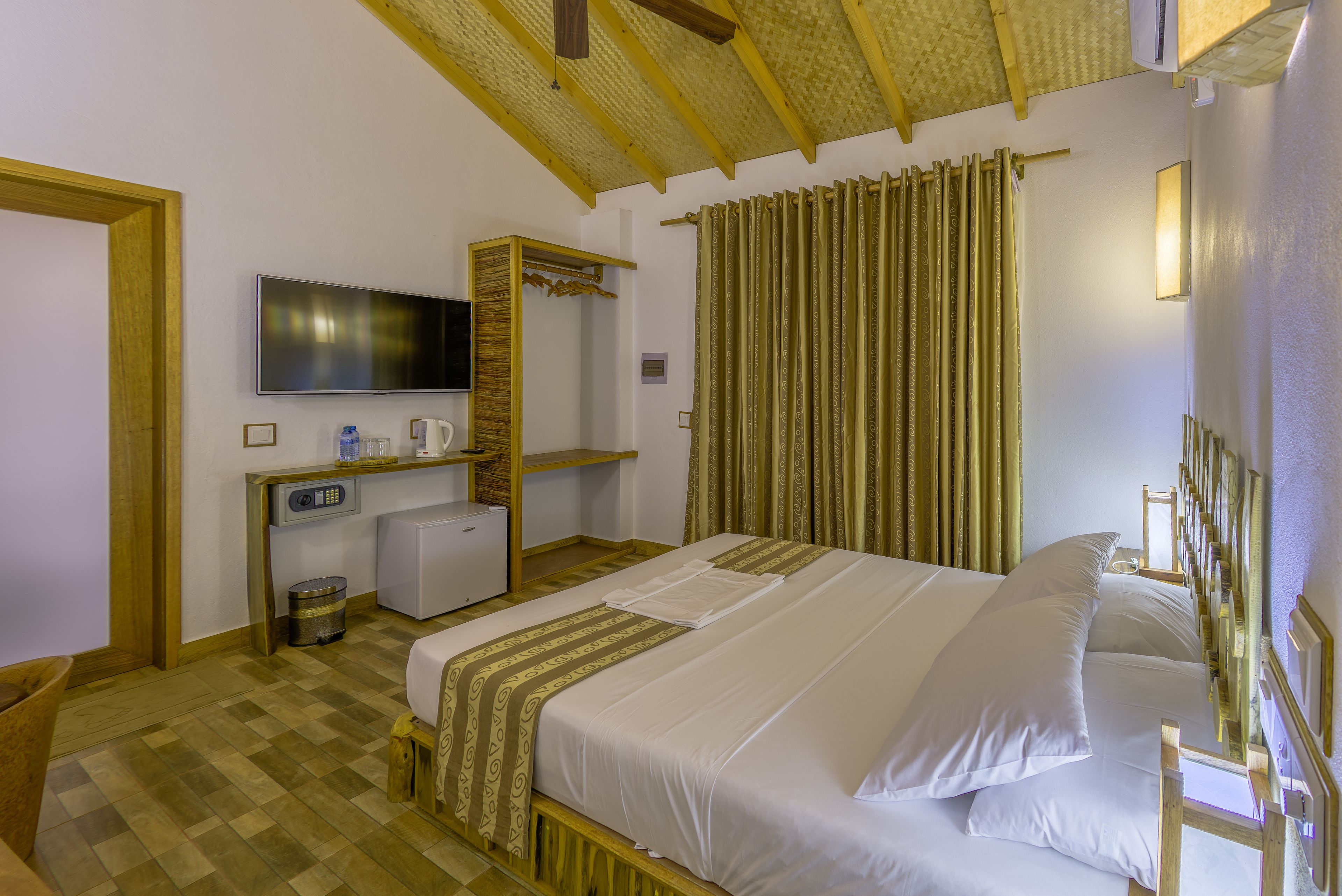 A hotel room with a large bed, a television, a desk with a computer, and a mirror.