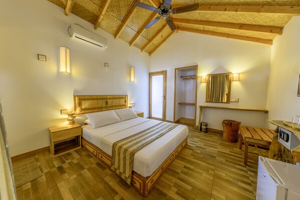 A spacious bedroom with a wooden ceiling, a large bed, bedside tables, a wooden bench, and a small kitchenette. - Ameera Maldives (Dhiffushi)