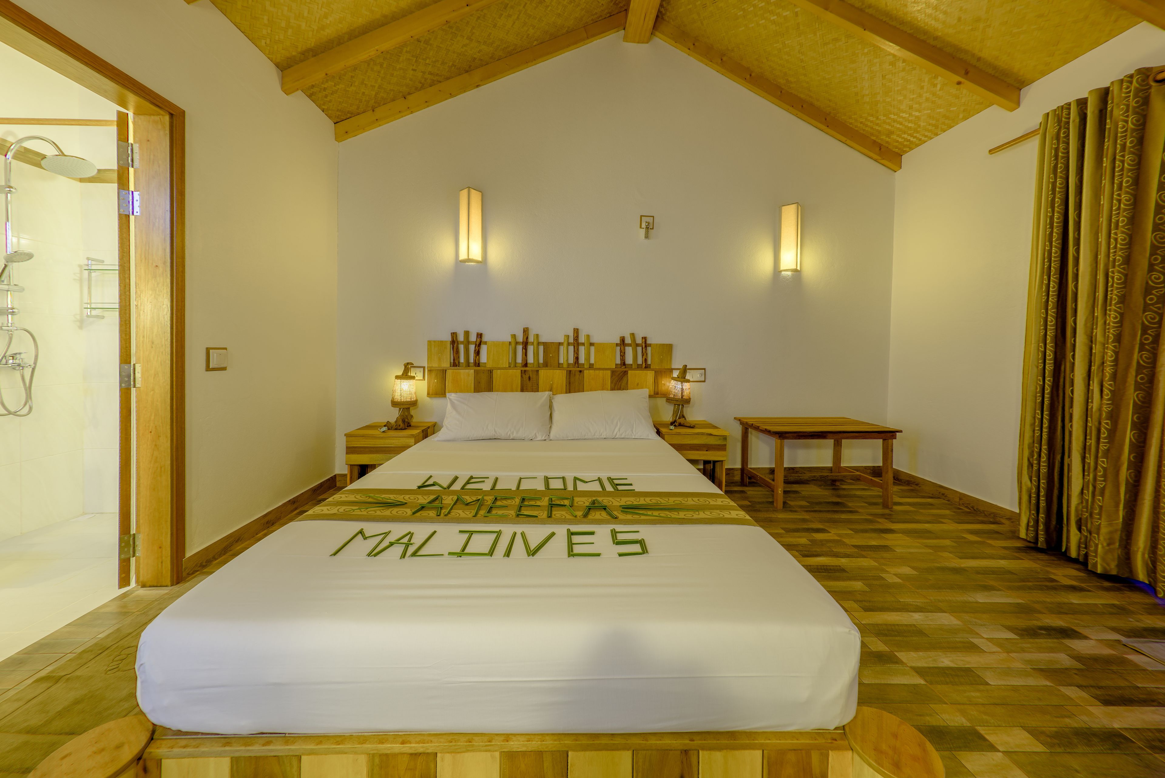 A hotel room with a bed, wooden headboard, bedside tables, and a small table. The bed has a welcome message.