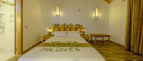 A hotel room with a bed, wooden headboard, bedside tables, and a small table. The bed has a welcome message.