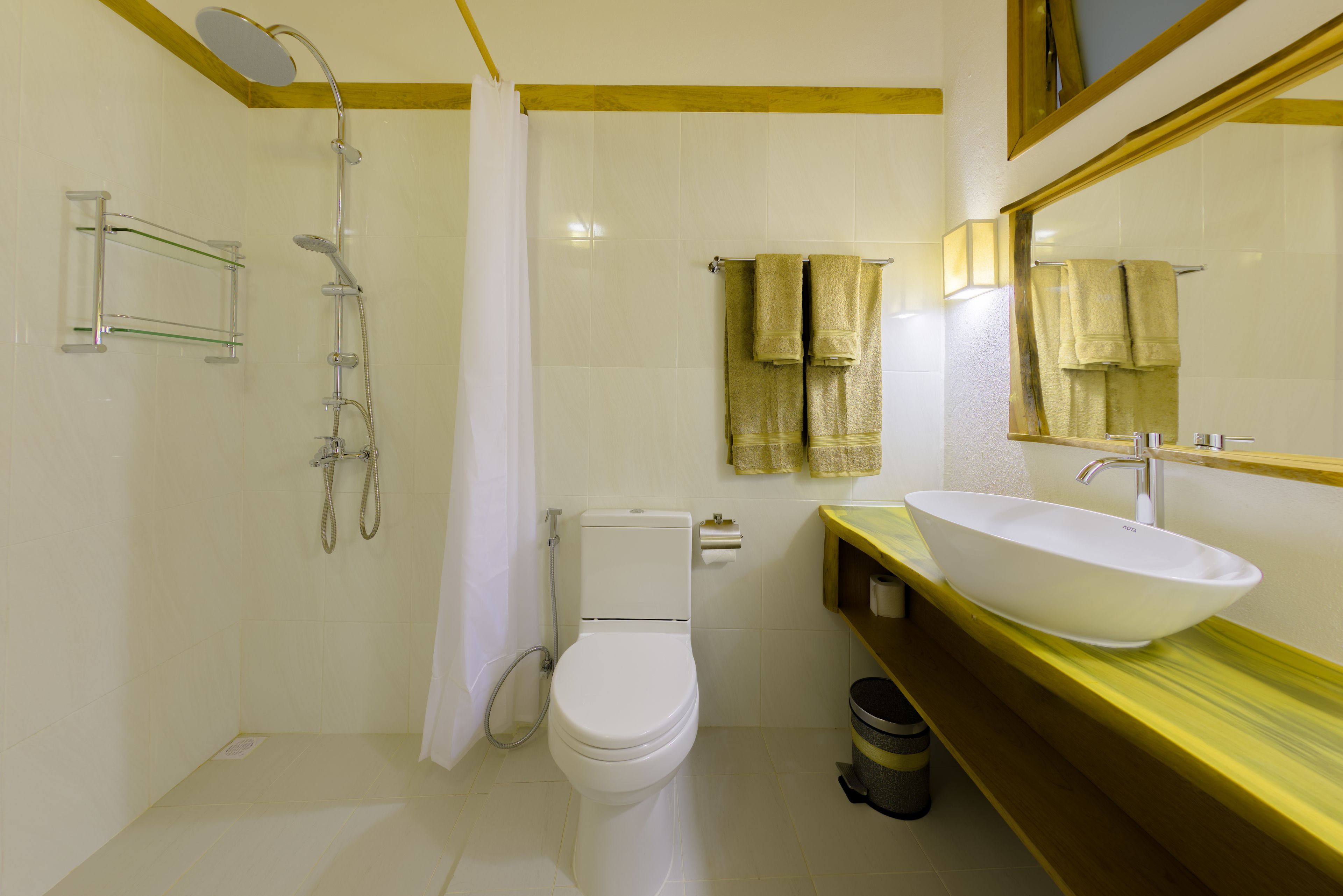 Une salle de bain avec des toilettes blanches, une douche, un lavabo avec un grand bac et des serviettes suspendues à un porte-serviettes.