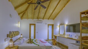 Een slaapkamer met een houten plafond, een bed met een witte dekbedovertrek, nachtkastjes met decoratieve objecten, een kleine koelkast, en een houten plank met een spiegel en een televisie.