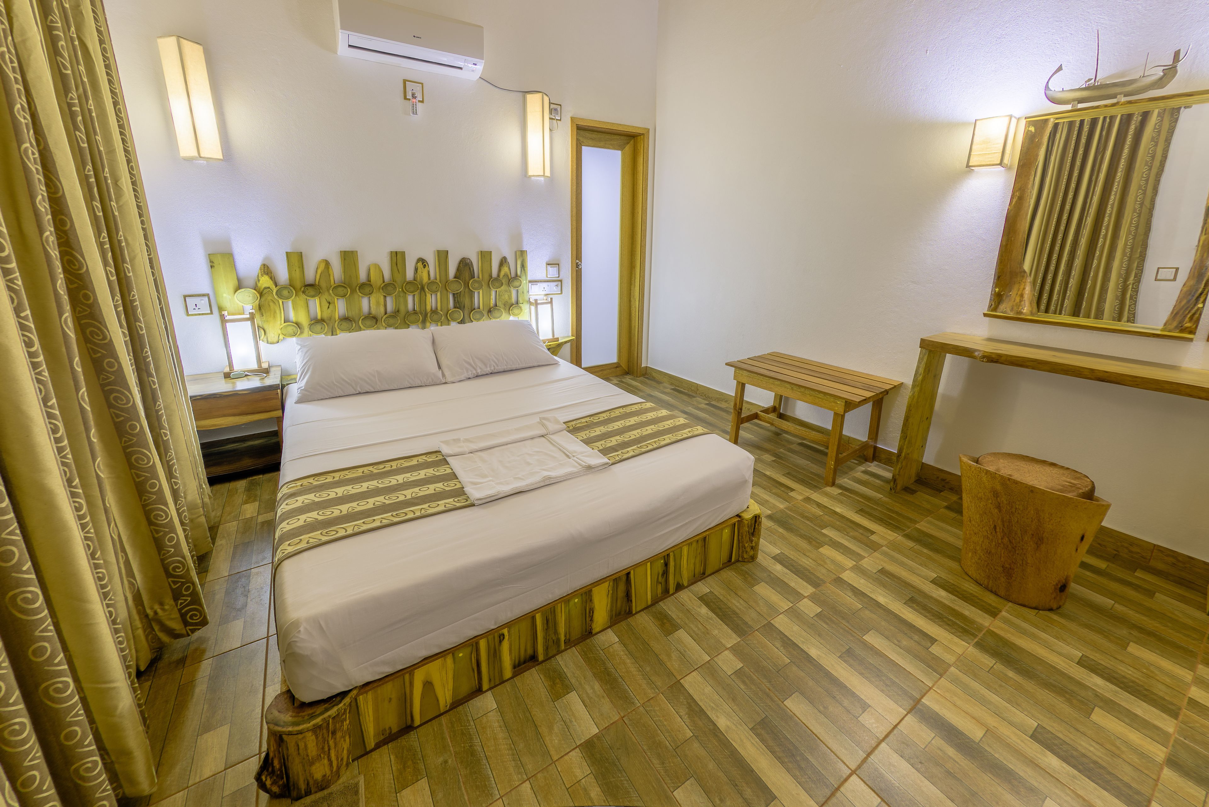 Una habitación de hotel con cama, mesita de noche, espejo y suelo de madera.