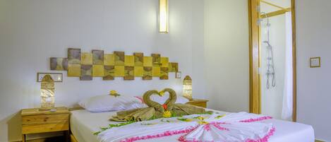 A neatly made bed with a heart-shaped towel arrangement, a wooden headboard with a geometric pattern, and a wooden nightstand with a lamp.