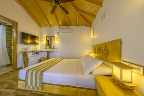 A hotel room with a wooden ceiling, a bed with white linens, a bedside table with a lamp, a small desk with a mirror, and an air conditioning unit on the wall. - Ameera Maldives (Dhiffushi)