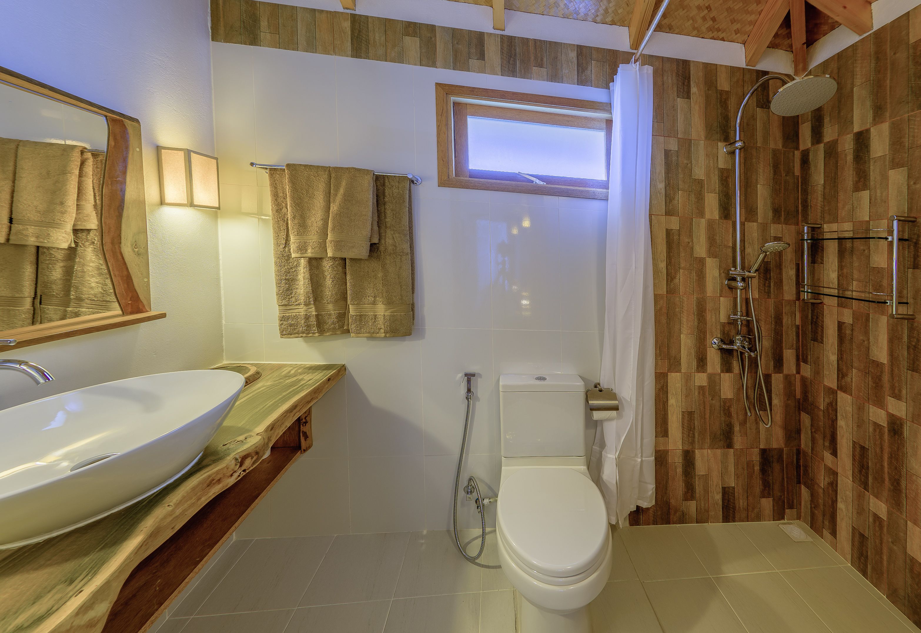 A bathroom with a wooden vanity, a white sink, a toilet, and a shower area.
