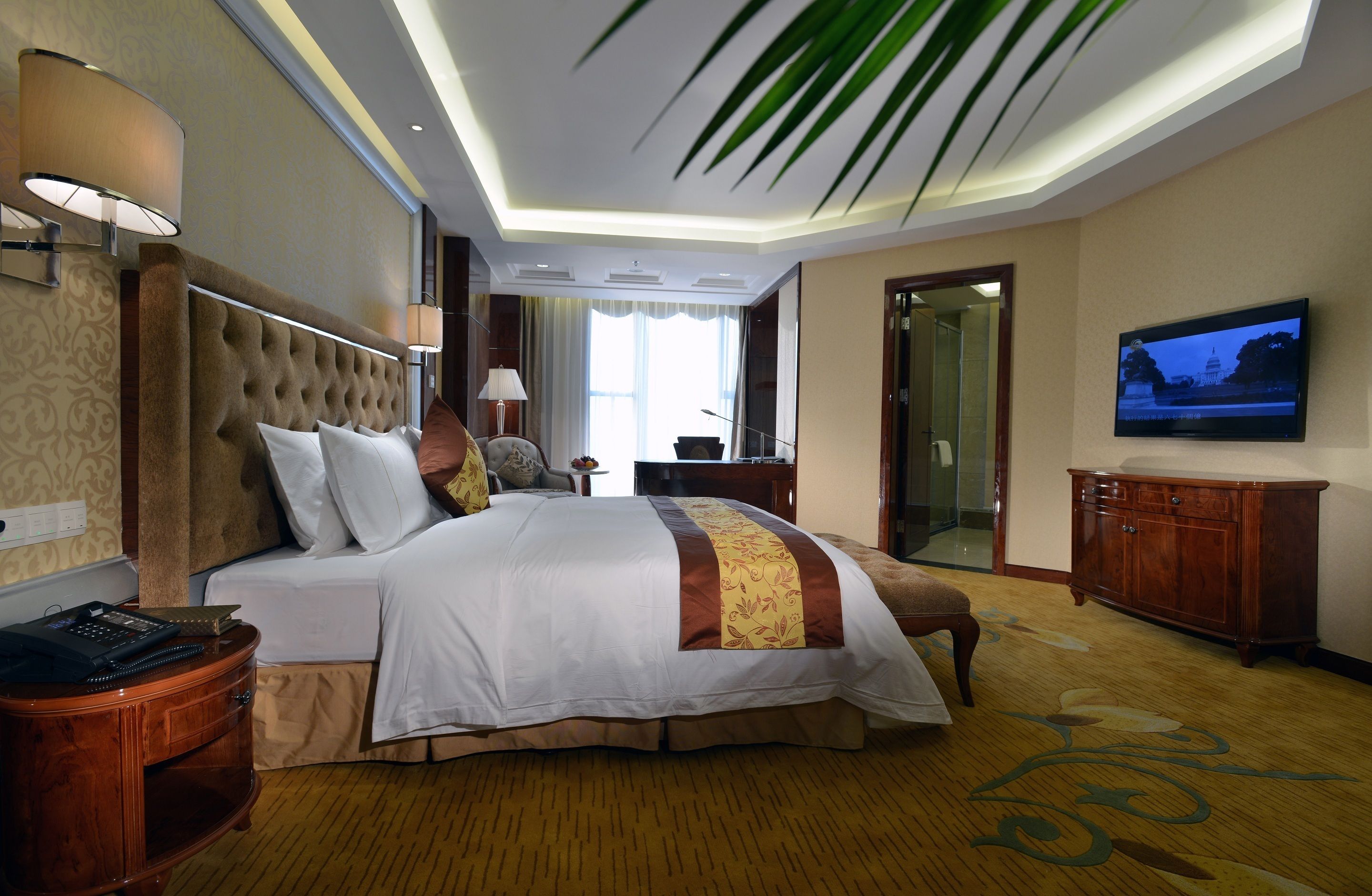 A hotel room with a large bed, a television, a wooden cabinet, and a desk with a lamp.