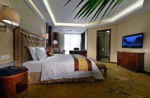 Une chambre d’hôtel avec un grand lit, une télévision, une armoire en bois et un bureau avec une lampe.
