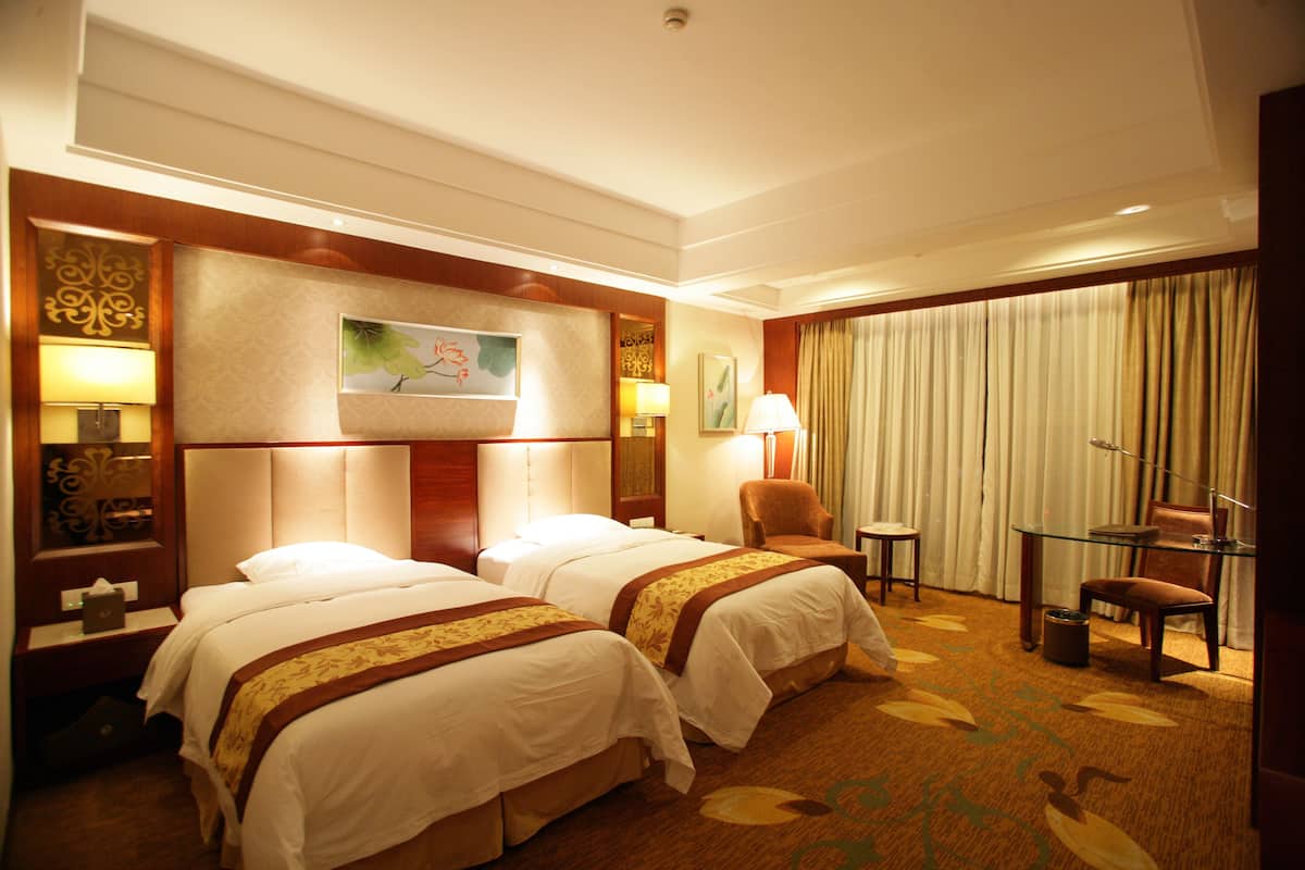 Habitación de hotel con dos camas, un escritorio, una silla, una lámpara y una ventana con cortinas.