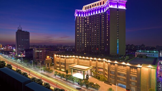 A high-rise hotel with a prominent lit top, surrounded by other buildings and a busy street. - Huilihua Hotel (Dongguan)