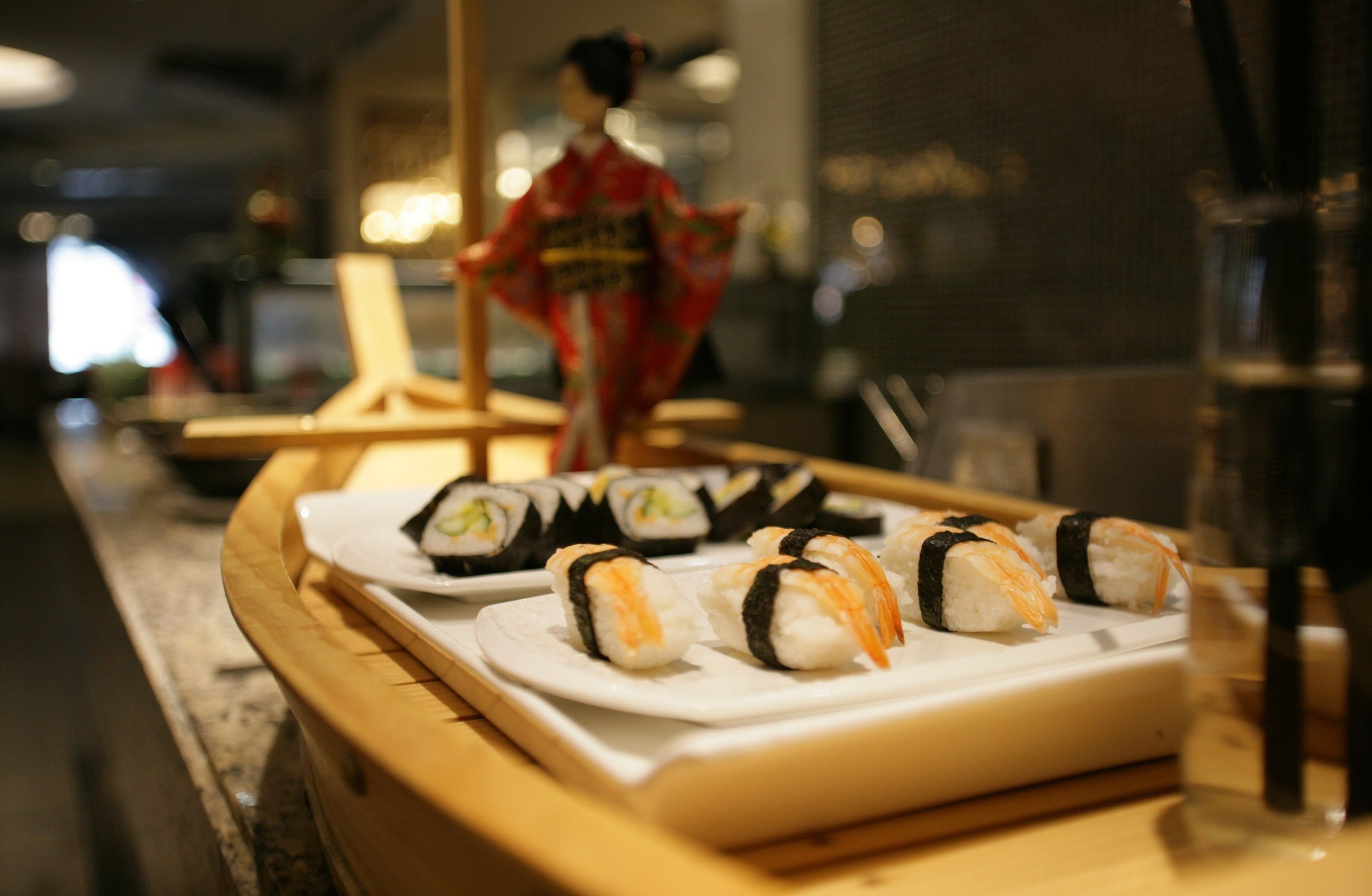 Sushi on a wooden tray with a decorative figure in the background.
