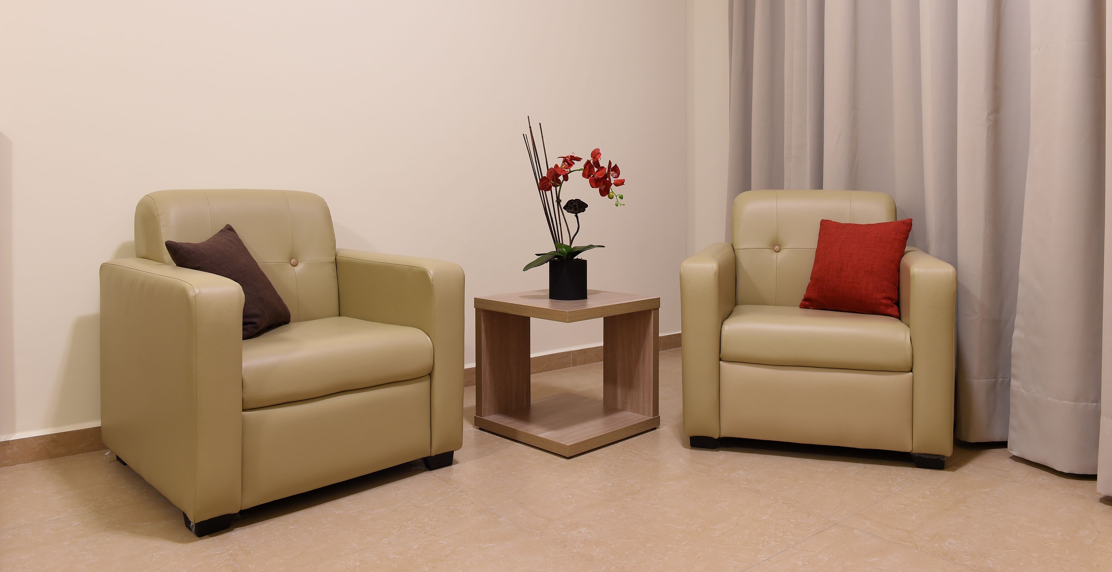 Dos sillones color beige con cojines, una pequeña mesita de madera y una planta en maceta con flores rojas.