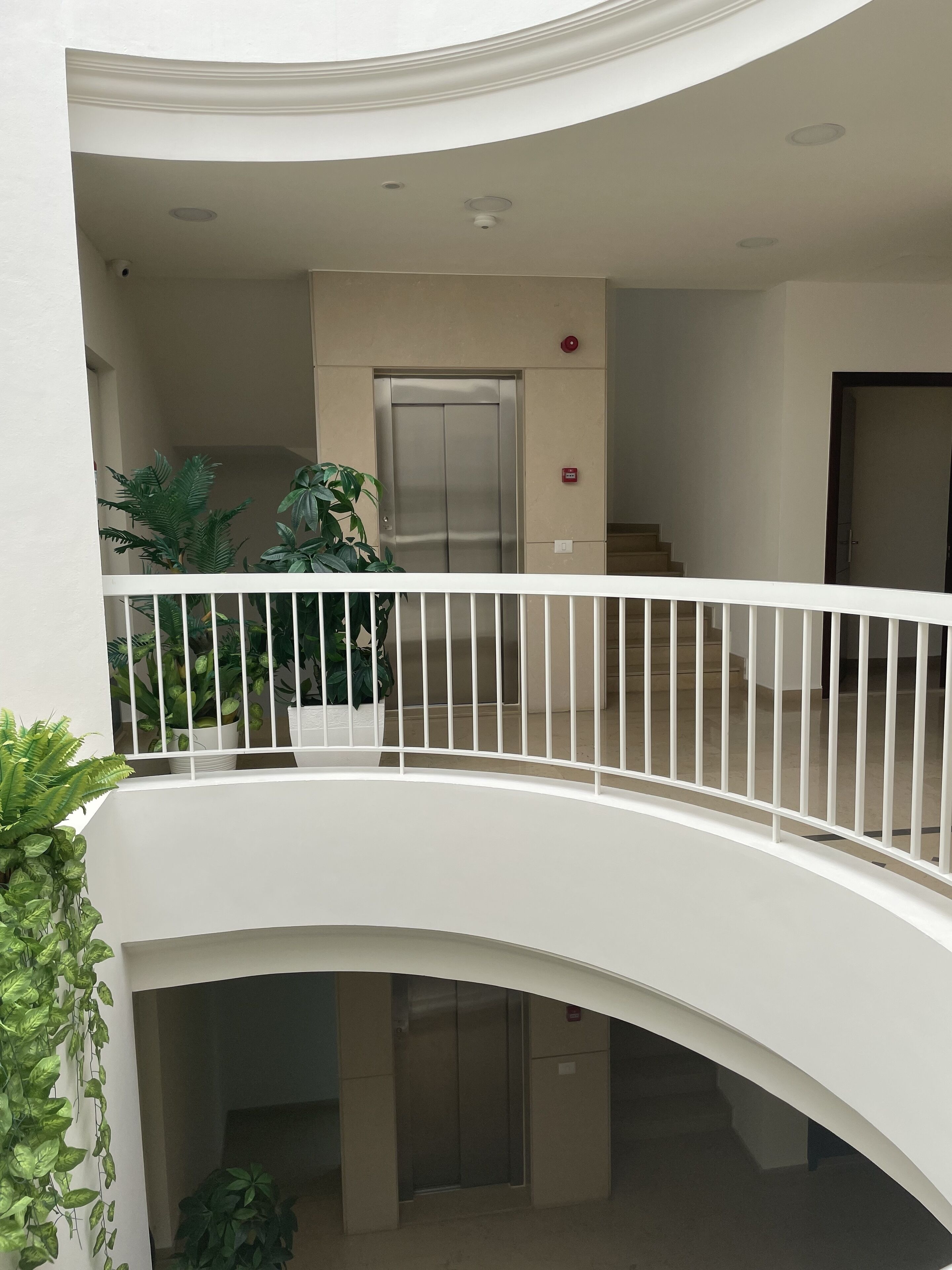 A multi-level building with a white balcony railing, an elevator, and potted plants.