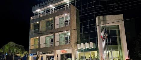 A modern hotel with a prominent 'Byblos Hotel' sign, multiple floors, and a well-lit entrance.