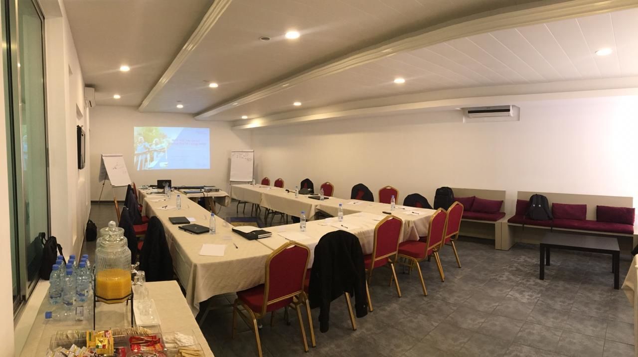 A conference room with long tables, red chairs, and a projector screen.