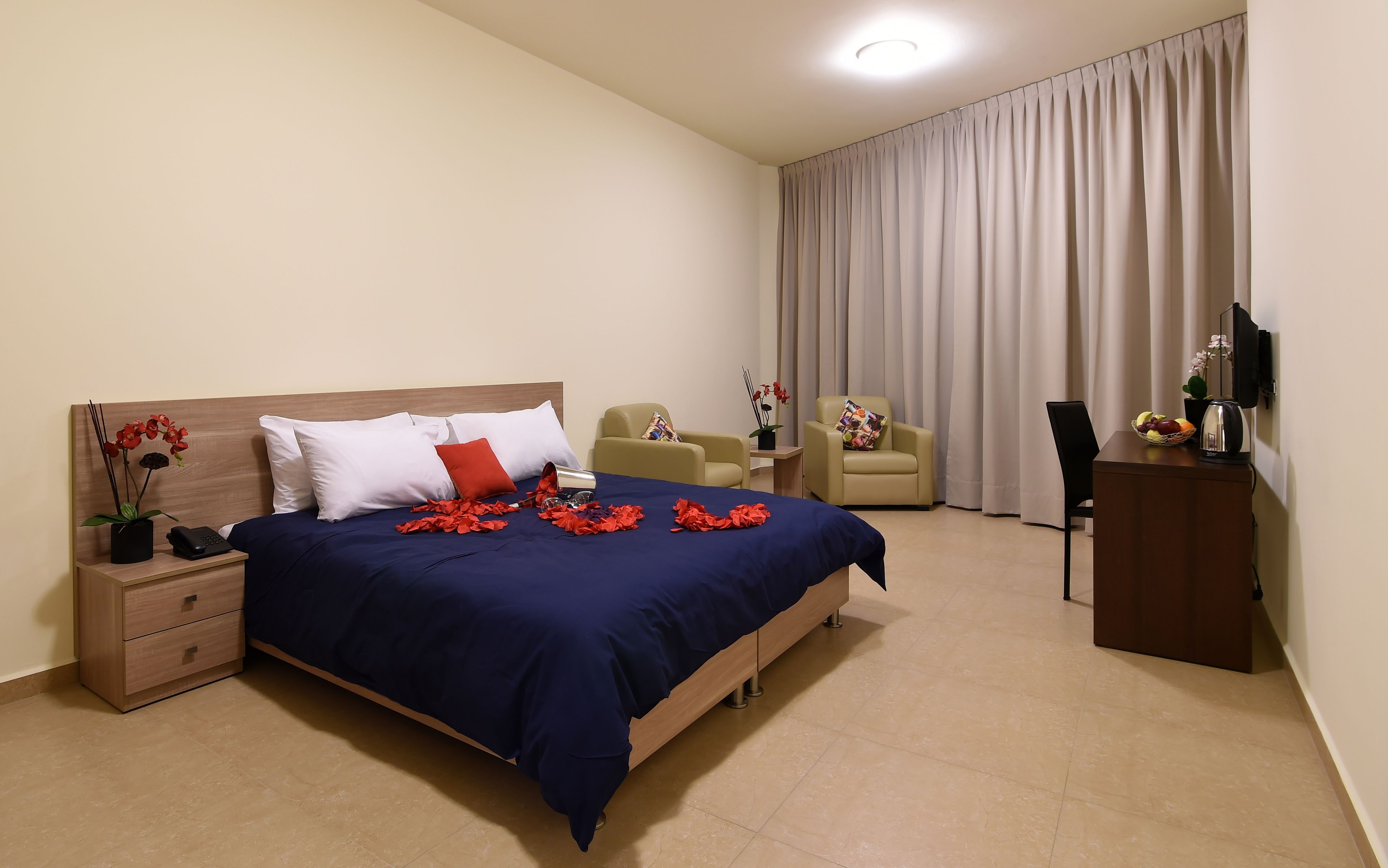 Una habitación de hotel con una cama, dos sillas, un escritorio con un hervidor y un televisor.