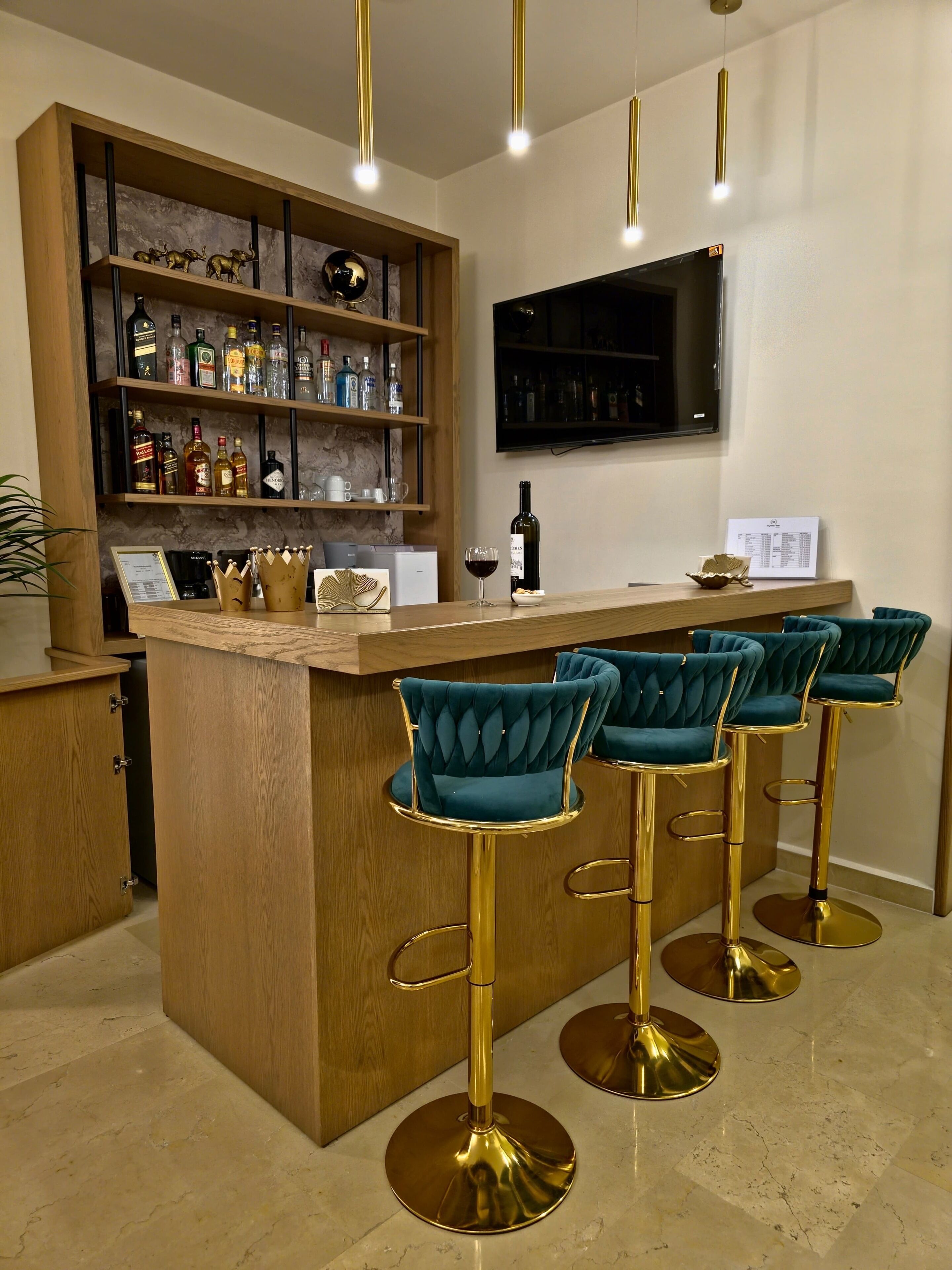 Zona de bar con mostrador de madera, taburetes y estante con botellas de licores.