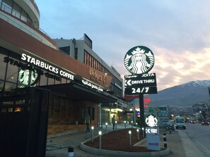 A Starbucks Coffee and Delora Hotel & Suites sign, a drive-thru sign, and a mountain in the background. - Delora Hotel and Suites (Chtaura)