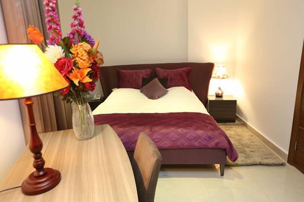 Une chambre à coucher bien rangée, avec un lit, des tables de chevet, une lampe et un vase de fleurs.