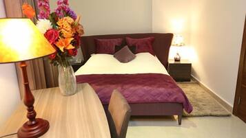 A neatly arranged bedroom with a bed, bedside tables, a lamp, and a vase of flowers.