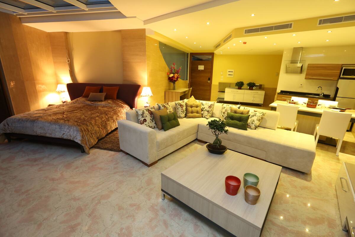 Une chambre d’hôtel moderne dotée d’un grand lit, de deux canapés, d’une table basse et d’une kitchenette.