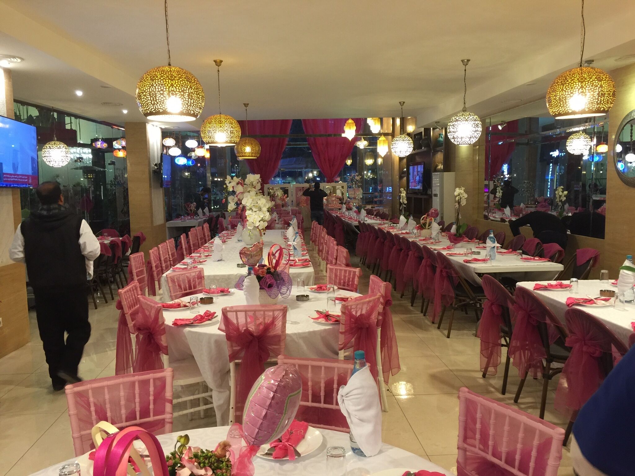 A banquet hall with long tables, pink chairs, and decorative lighting.