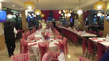 A banquet hall with long tables, pink chairs, and decorative lighting.