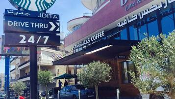 Un hotel con el logotipo de Starbucks Coffee, un acceso para autos y un anuncio que indica servicio las 24 horas, los 7 días de la semana.